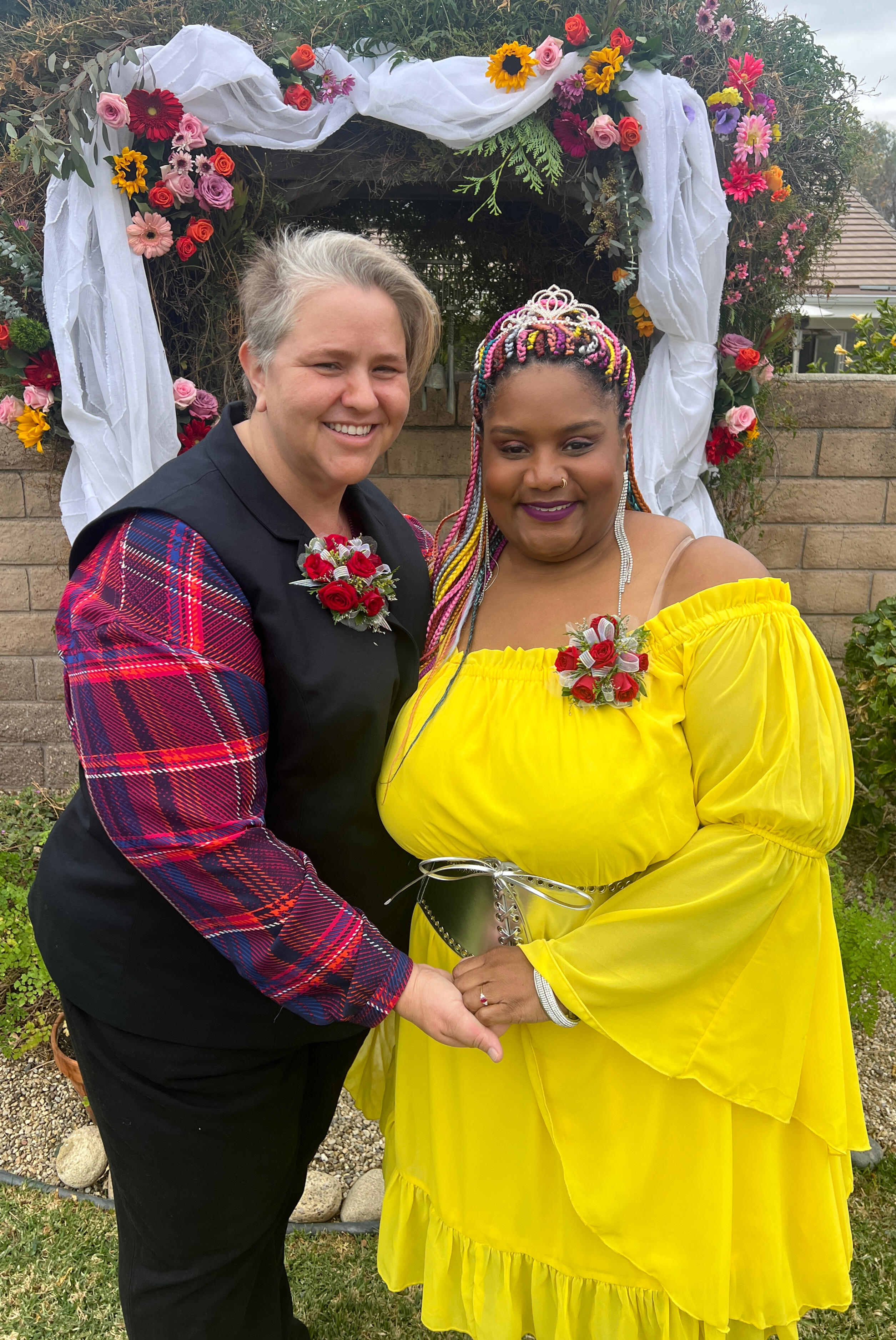 My wedding day! Two women celebrating their wedding day. One bride in a black suit and one bride in a bright yellow dress with a tiara.